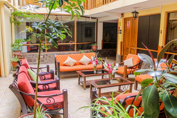 A spacious indoor seating area with a sofa, chairs, and tables, surrounded by potted plants.