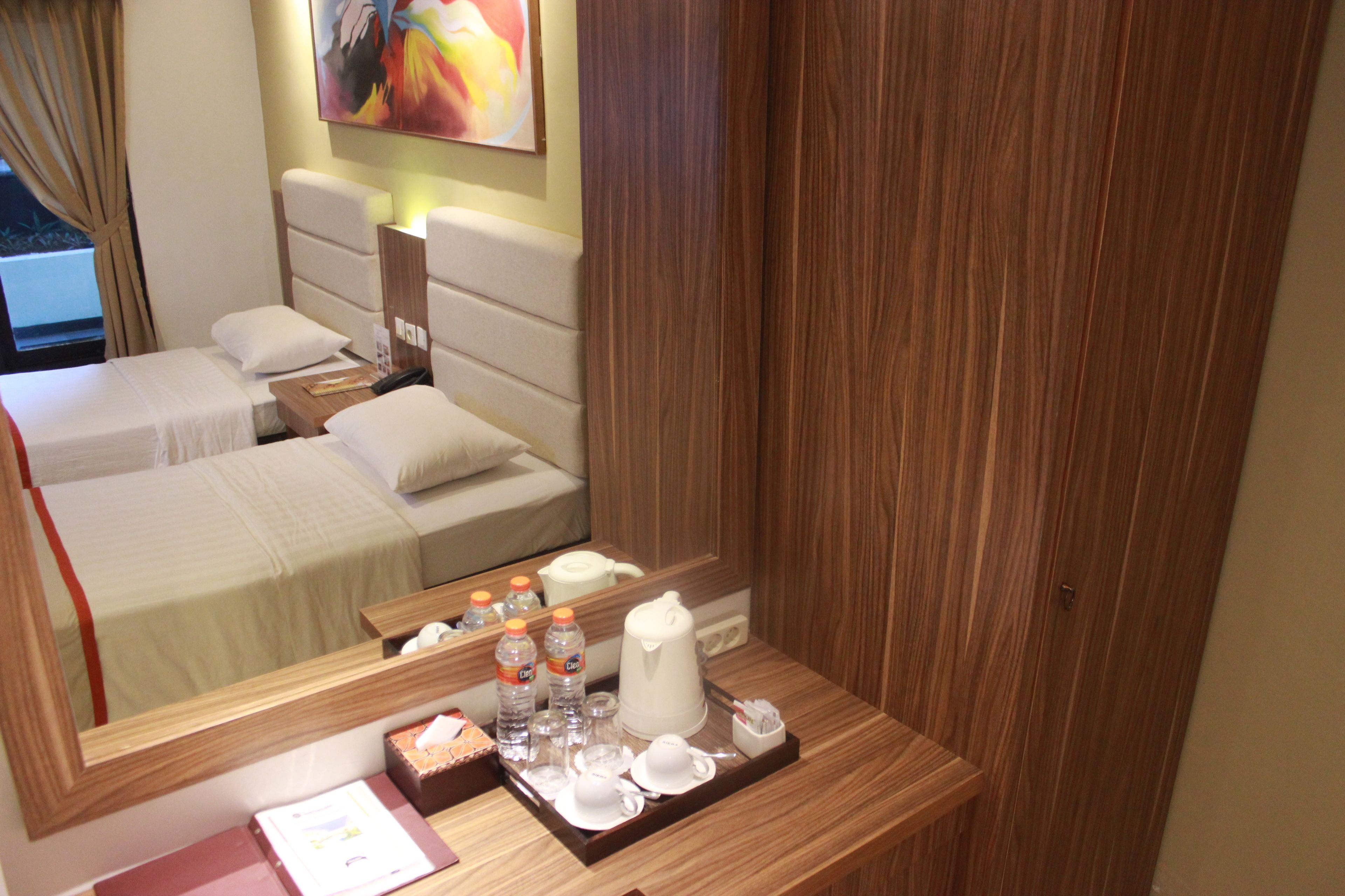 A hotel room with a bed, a bedside table with toiletries, a mirror, and a wooden wardrobe.
