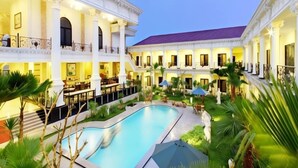 A hotel with a swimming pool surrounded by lush greenery and a covered outdoor seating area. - The GRAND PALACE Hotel - YOGYAKARTA (Yogyakarta)