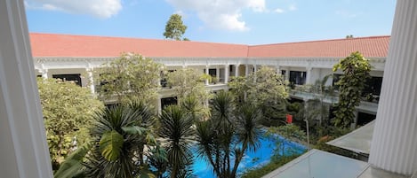 A courtyard with a swimming pool surrounded by lush greenery and a building with a red-tiled roof.