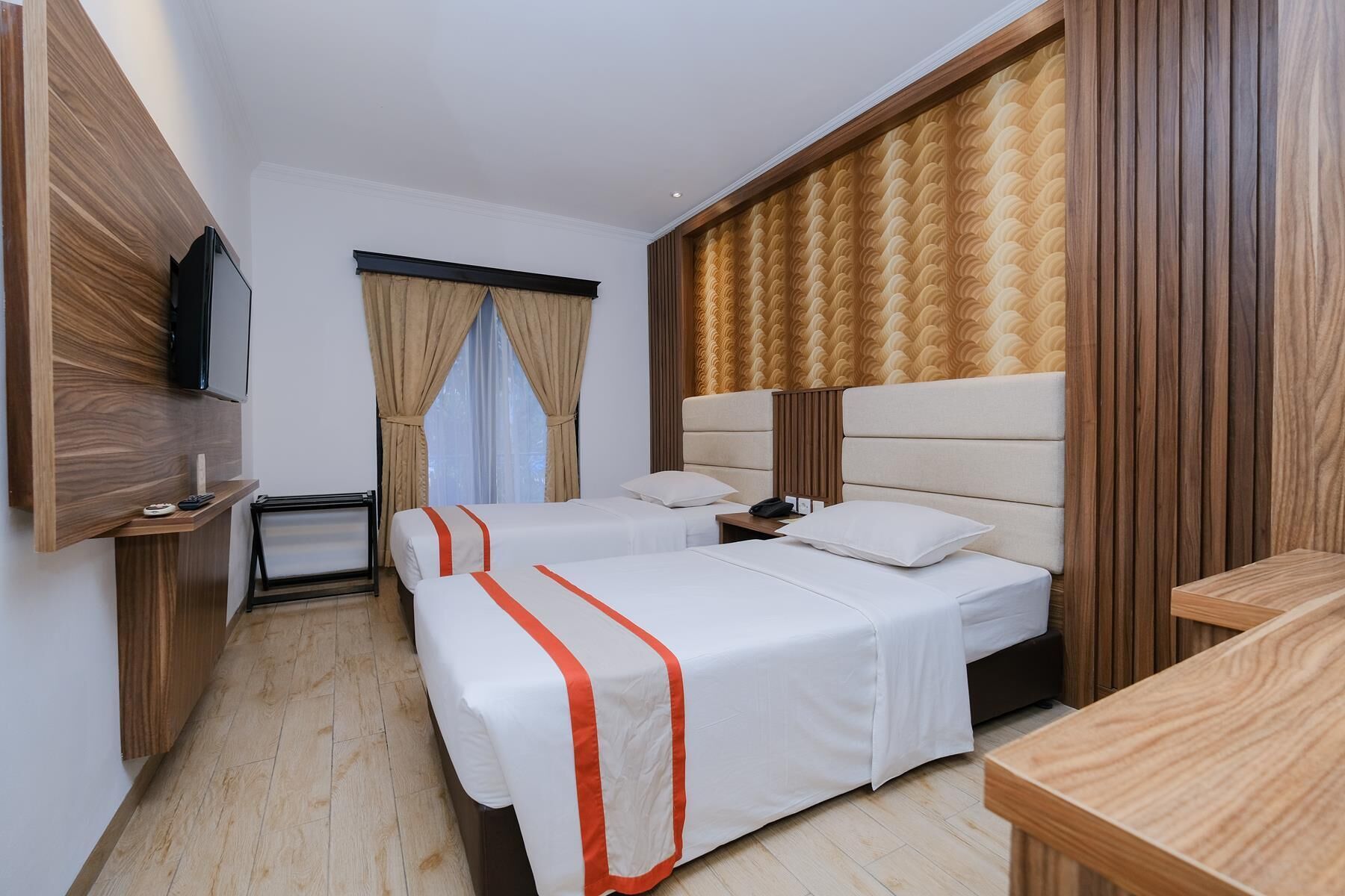 Habitación de hotel con dos camas, televisión, escritorio y ventana con cortinas.