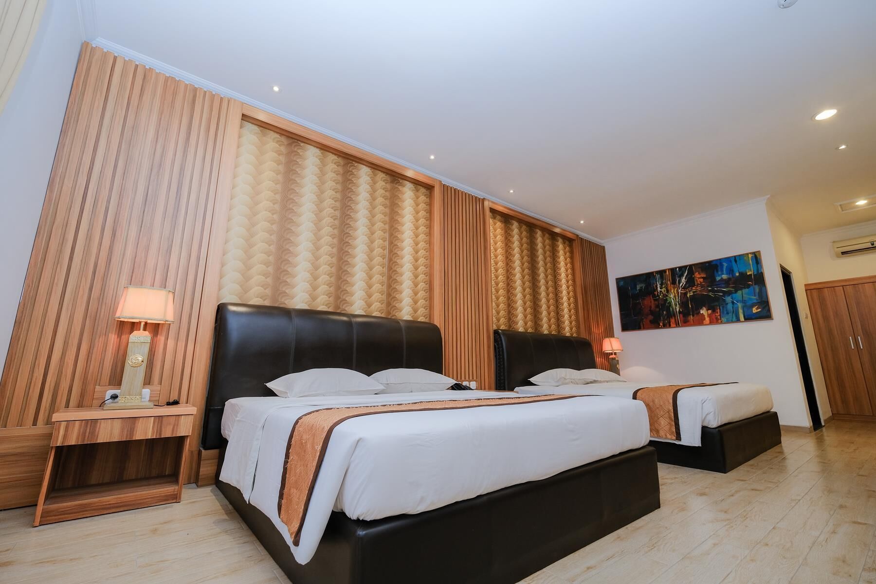 Una habitación de hotel con una cama grande, dos mesitas de noche, un cuadro en la pared y un equipo de aire acondicionado.