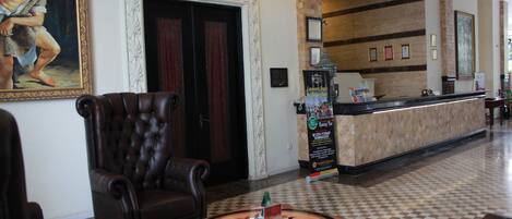 A lobby with a reception desk, a large framed painting, a dark leather armchair, and a checkered floor.