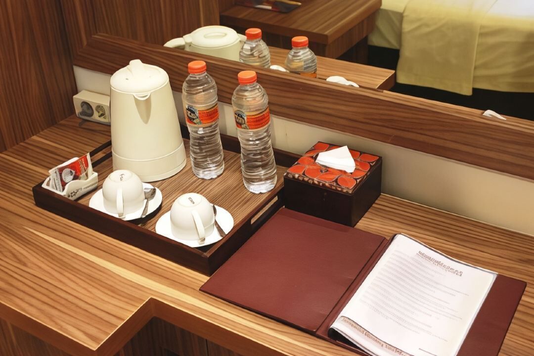 Quarto de hotel com escrivaninha de madeira, cafeteira, duas garrafas de água, caixa de lenços e menu.