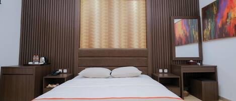 A hotel room with a large bed, wooden headboard, two nightstands, a bedside table, a large window with curtains, and a colorful abstract painting on the wall.