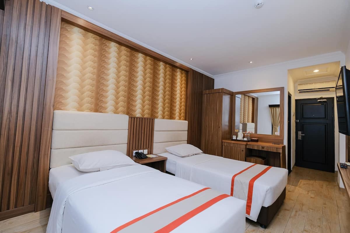 Een hotelkamer met twee bedden, een houten hoofdbord, een kaptafel met spiegel en een deur.