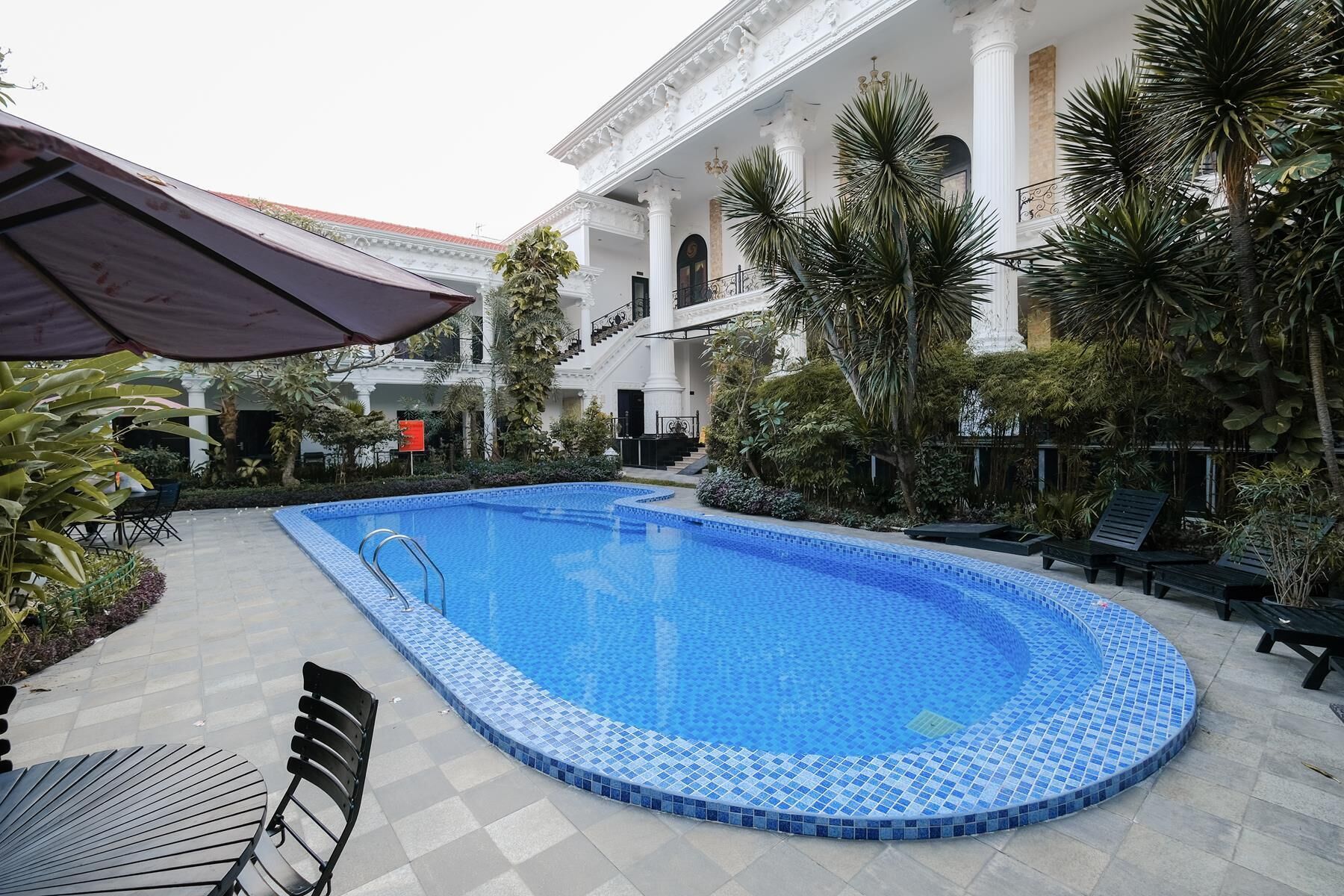 Una piscina con borde de azulejos, rodeada por un patio con sillas y una mesa.