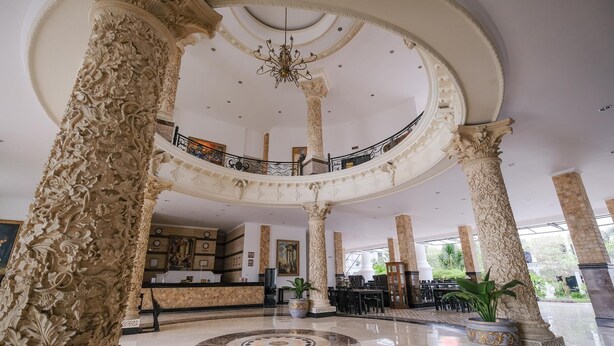 A grand lobby with ornate columns, a central circular floor design, and a staircase leading to an upper level. - The GRAND PALACE Hotel - YOGYAKARTA (Yogyakarta)