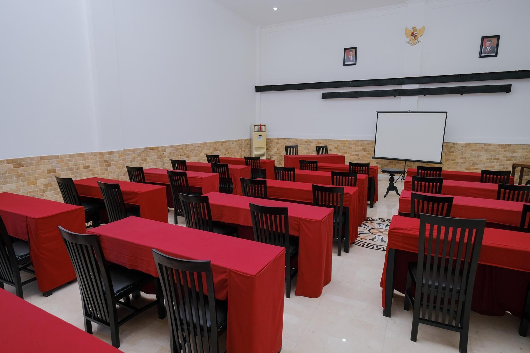 Un salón de conferencias con varias mesas y sillas, una pizarra y una pantalla para proyector.