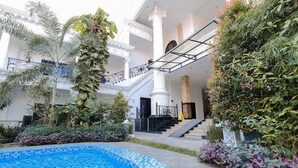 A pool area with a tiled edge, surrounded by lush greenery and a grand staircase leading to upper floors. - The GRAND PALACE Hotel - YOGYAKARTA (Yogyakarta)