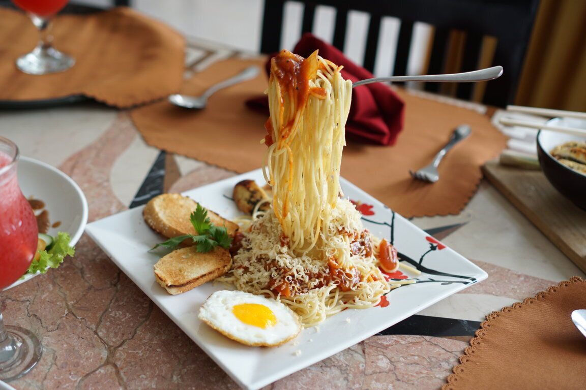 A plate of spaghetti with tomato sauce, a fried egg, and toasted bread on a table.
