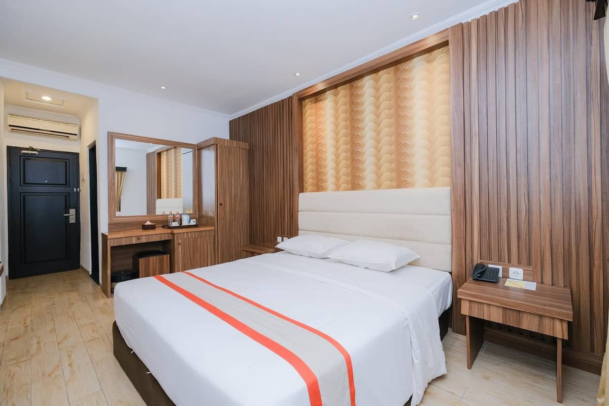 Een hotelkamer met een groot bed, een houten hoofdbord, een nachtkastje met een telefoon en een spiegel boven de kapstok.