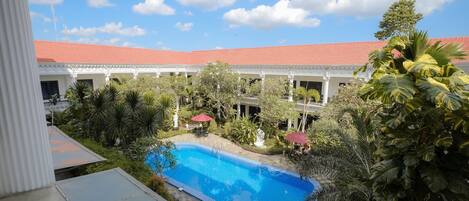 Un patio de hotel con piscina, abundante vegetación y un edificio de techo rojo.