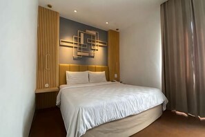 A hotel room with a bed, a headboard, a wall-mounted light fixture, and a window with curtains. - Best Hotel Kedungsari (Surabaya)