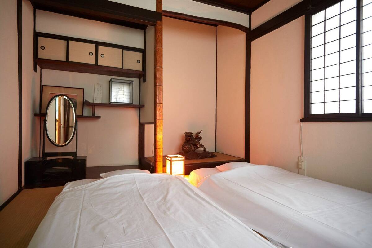 Quarto japonês tradicional com duas camas, um armário de madeira, um espelho e uma janela com venezianas em grade.
