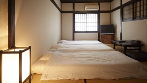 Una habitación tradicional japonesa con suelo de tatami, un futón, una mesa baja con una silla y una puerta corredera.