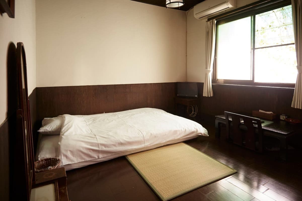 Quarto com cama, uma pequena mesa com televisão e janela com cortinas.