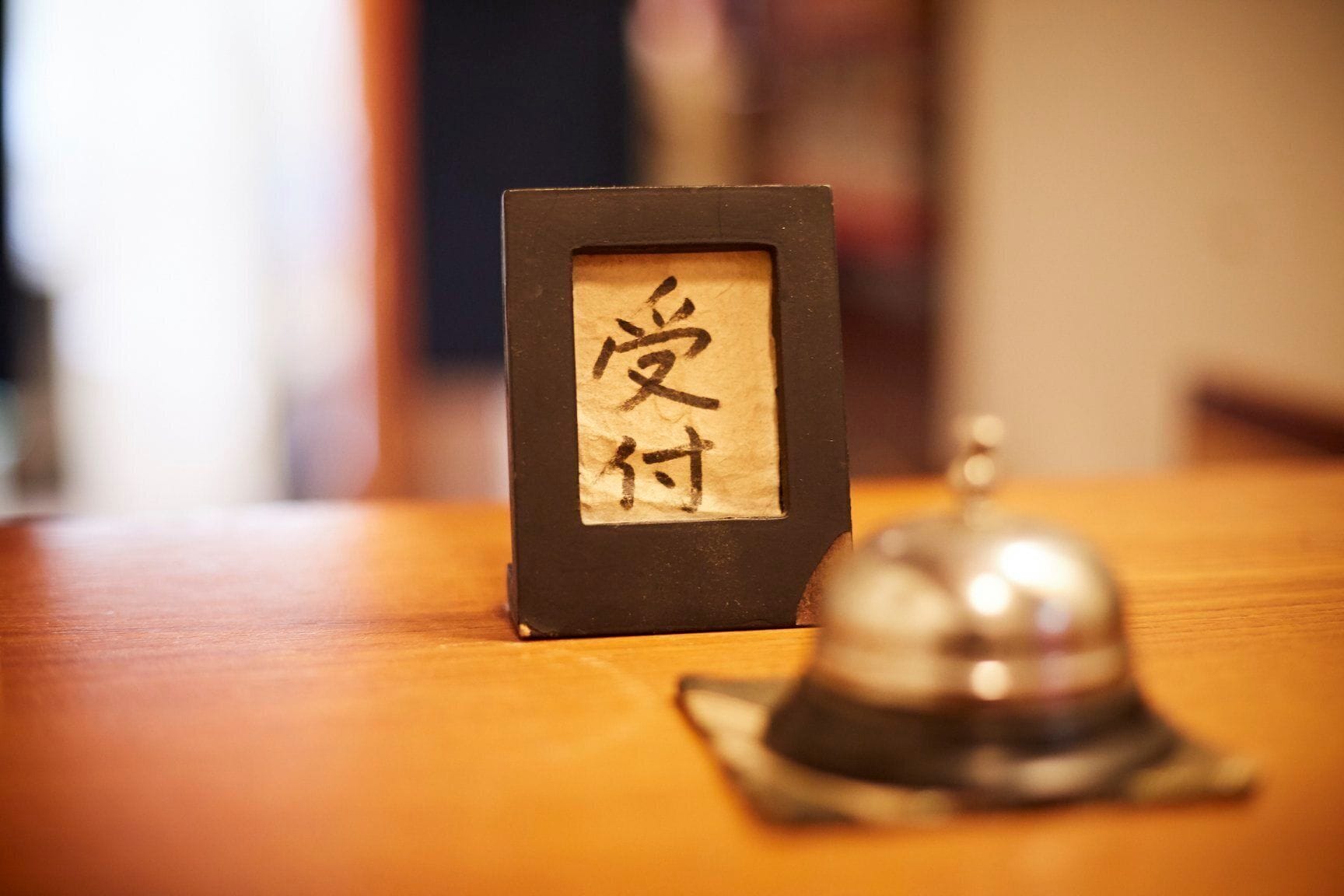 A framed calligraphy piece with Japanese characters on a wooden table, accompanied by a traditional bell.