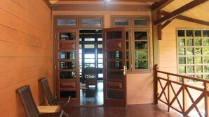 A wooden cabin with a porch, a dining area with chairs, and a large window. - Villa Del Porto (Langkawi)