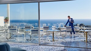 Un comedor moderno con vista al océano, que cuenta con sillas y mesas blancas y azules, además de un amplio ventanal de vidrio.