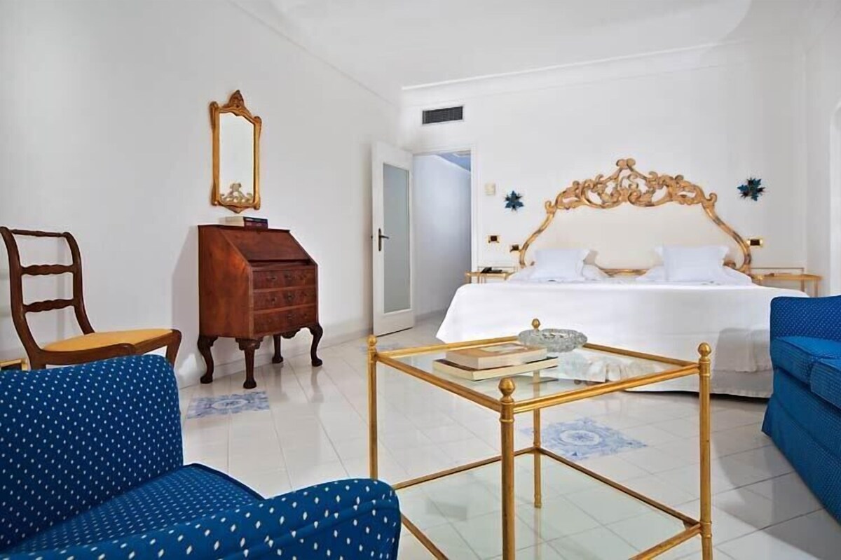 Un dormitorio con una cama, un tocador, una silla, un sofá y una mesita de cristal.