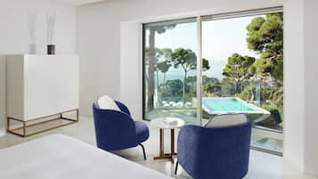 Una habitación moderna con un ventanal grande, dos sillas azules, una mesita redonda y un armario blanco.