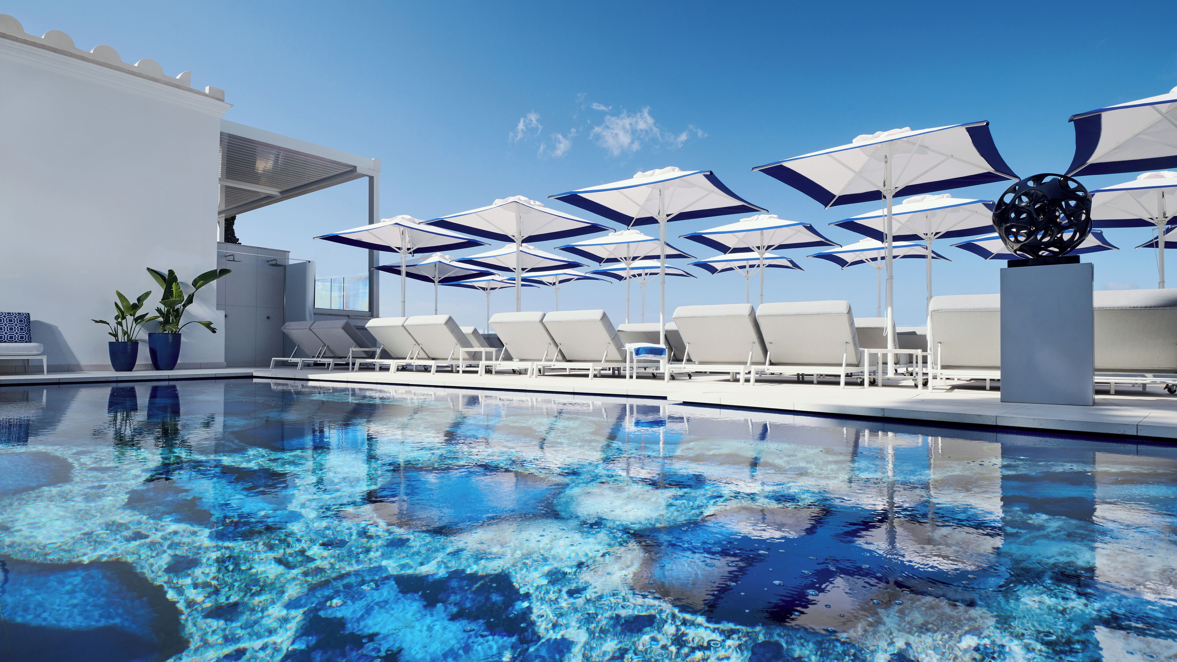 A poolside area with lounge chairs and umbrellas, a clear blue sky, and a modern building facade.