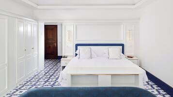 Ein Hotelzimmer mit einem großen Bett, weißen Wänden, einem blauen Kopfteil und gemusterten Bodenfliesen.