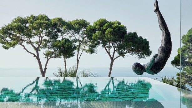 Una piscina con agua cristalina que refleja árboles y una escultura.