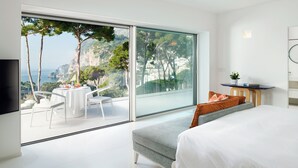 Un dormitorio moderno con un gran ventanal corredera que da a un balcón y vistas panorámicas de acantilados y el mar.