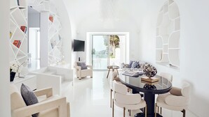 Un salón moderno con decoración blanca, una mesa de vidrio, asientos cómodos y vistas al exterior.