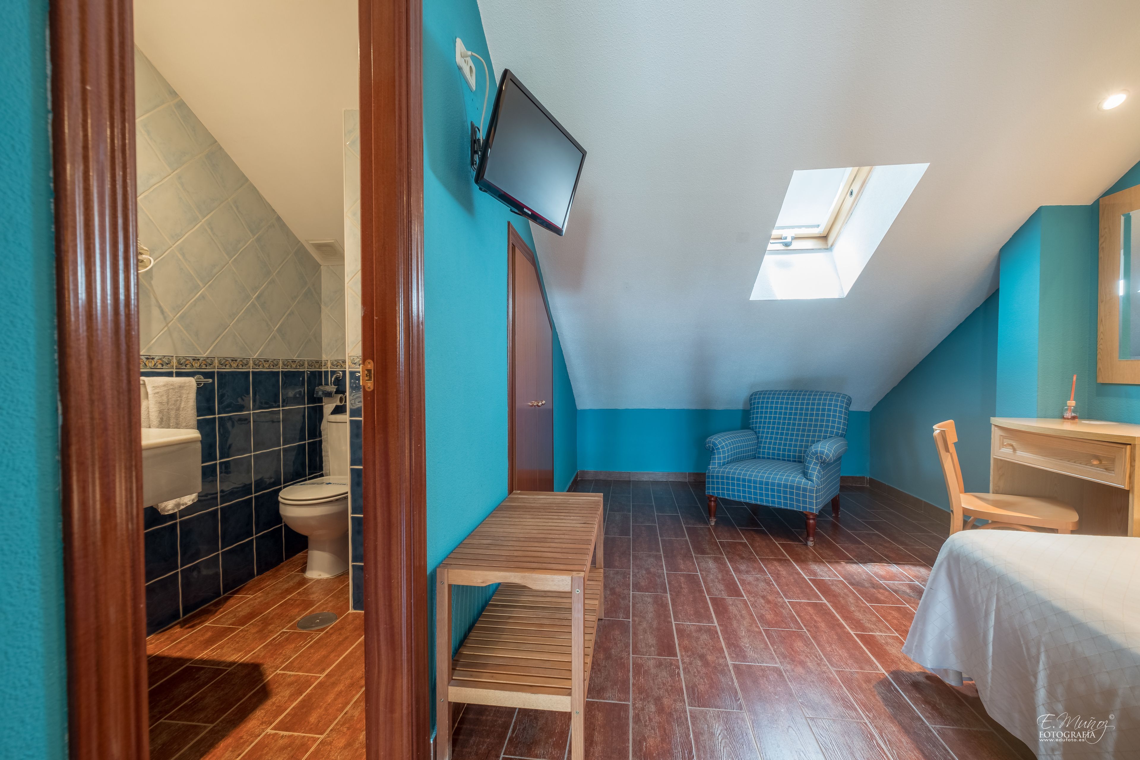 Ein Schlafzimmer mit Dachfenster, einem Bett, einem Schreibtisch, einem Stuhl und einem Badezimmer mit Toilette und Waschbecken.