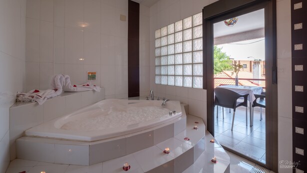 A modern bathroom with a large bathtub, a shower area, and a glass door leading to an outdoor seating area. - Hotel Vivar (Grinon)