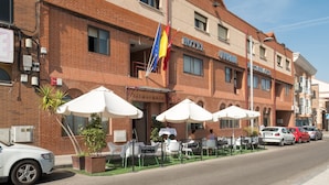A hotel with a brick facade, outdoor seating with umbrellas, and flags. - Hotel Vivar (Grinon)