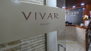 A reception area with a sign reading "VIVAR Hotel" and a brick wall in the background. - Hotel Vivar (Grinon)
