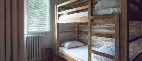 A bunk bed room with a rustic wooden design, a window with blinds, and a radiator.