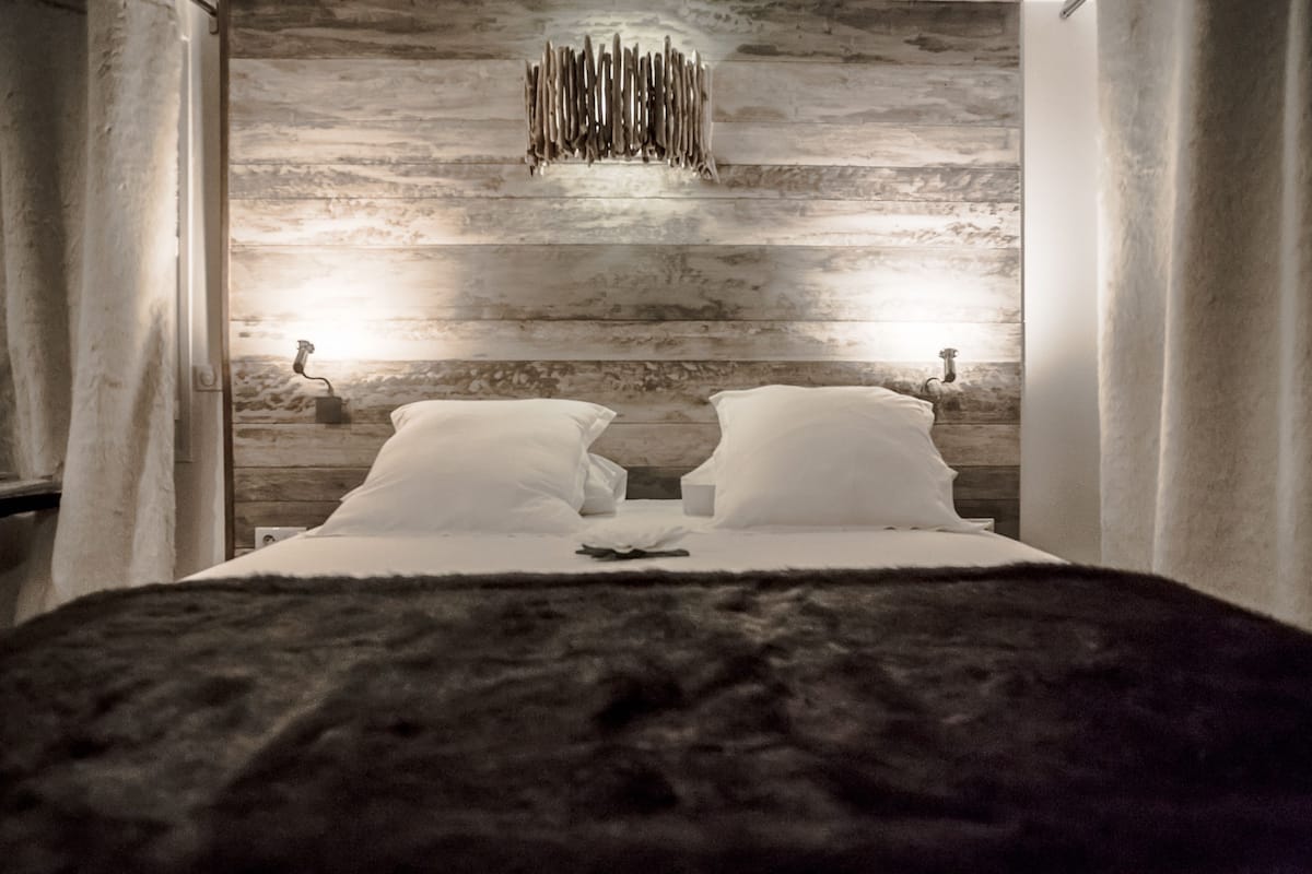 A bedroom with a wooden wall, two bedside tables with lamps, and a bed with white linens.