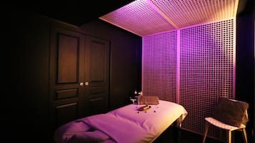 A dimly lit room with a bed, a chair, and a wall with a grid pattern.