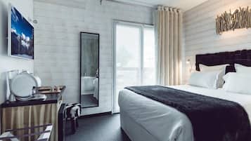 A modern hotel room with a large bed, a desk with a mirror, a wardrobe, and a window with curtains.