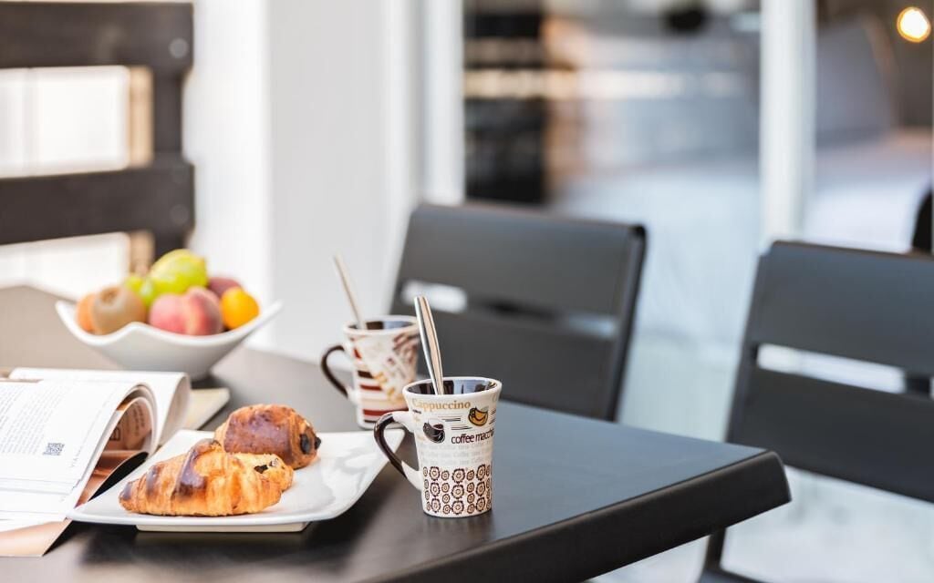 A table with croissants, a bowl of fruit, and two coffee mugs.