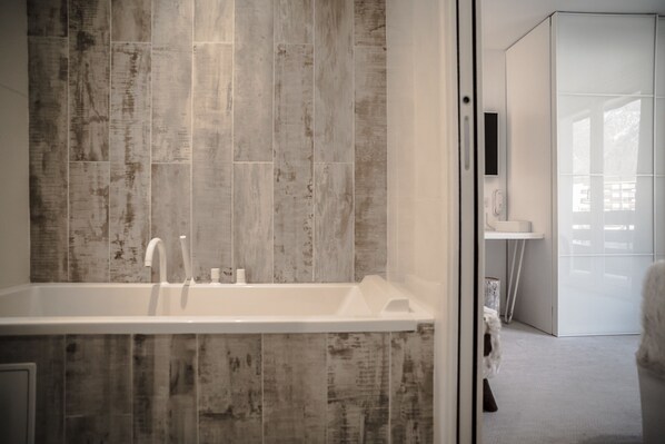 Un baño moderno con una bañera grande, revestimiento de madera en la pared, un lavabo blanco y una mampara de cristal.