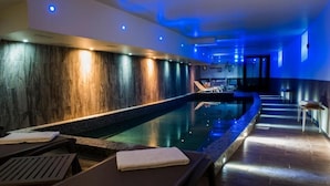 A modern indoor pool area with wooden walls, lounge chairs, and a long bench. - Rock Noir Hôtel & Spa (La Salle-les-Alpes)