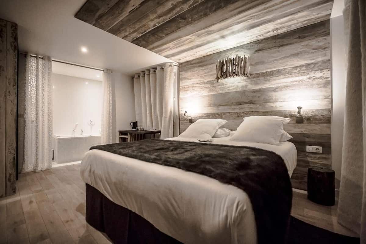 A modern bedroom with a large bed, wooden wall paneling, a built-in bench, and a window with curtains.