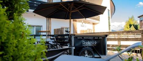 Un hotel con zona de estar cubierta al aire libre, una bicicleta y un cartel que indica que ofrece servicios de hotel, restaurante, bar y spa.