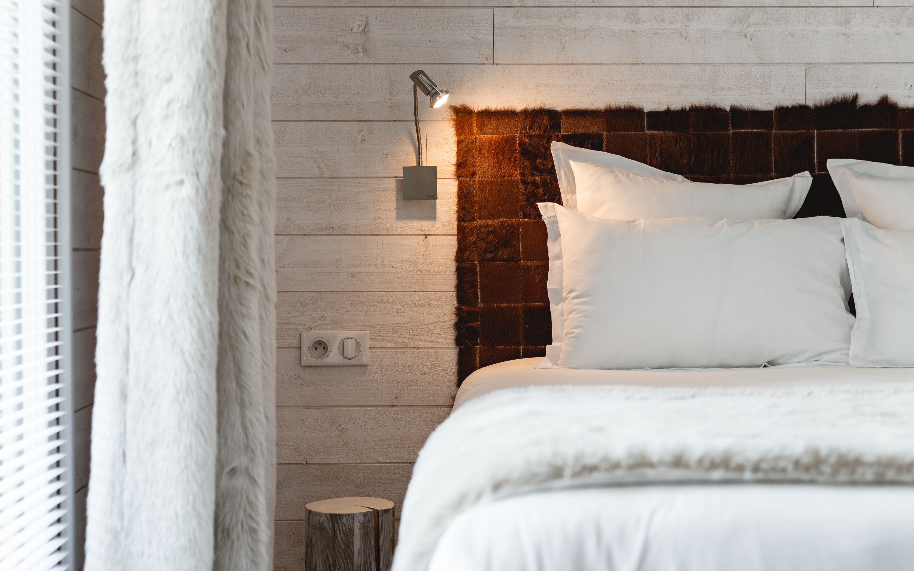 A bedroom with a wooden headboard, white bedding, a bedside lamp, and a power outlet.