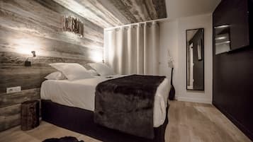Un dormitorio moderno con pared de madera, una cama con ropa de cama blanca, un plaid oscuro, una mesita de noche con una lámpara y un espejo en la pared.
