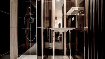 A modern bathroom with a glass-enclosed shower, a white pedestal sink, and dark tiled walls.