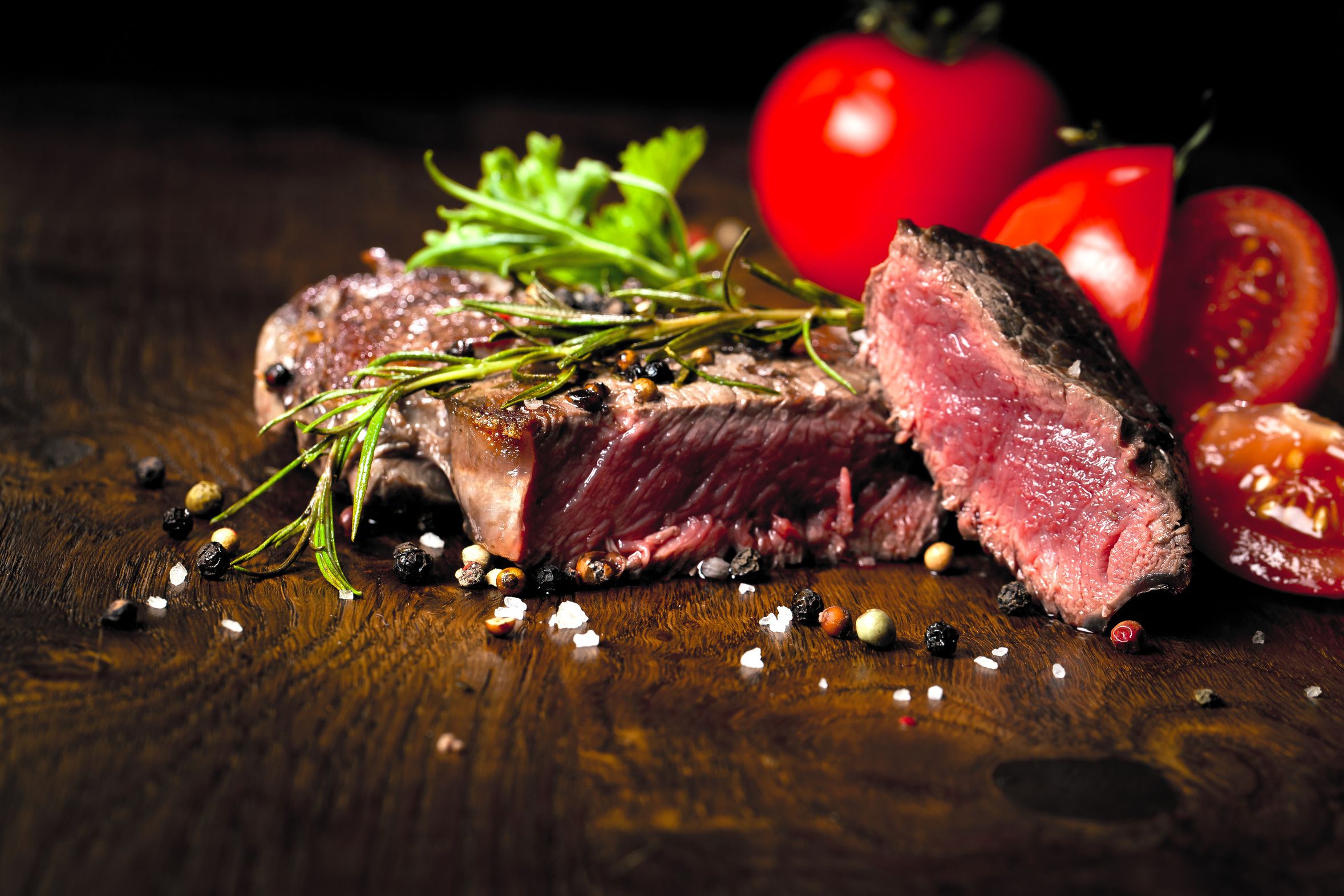 Bife com alecrim e grãos de pimenta sobre superfície de madeira.