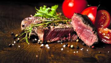 Bife com alecrim e grãos de pimenta sobre superfície de madeira.