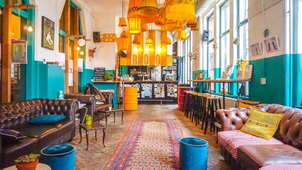 A cozy interior with leather sofas, a patterned rug, and hanging lamps. - Hostel ROOM Rotterdam (Rotterdam)